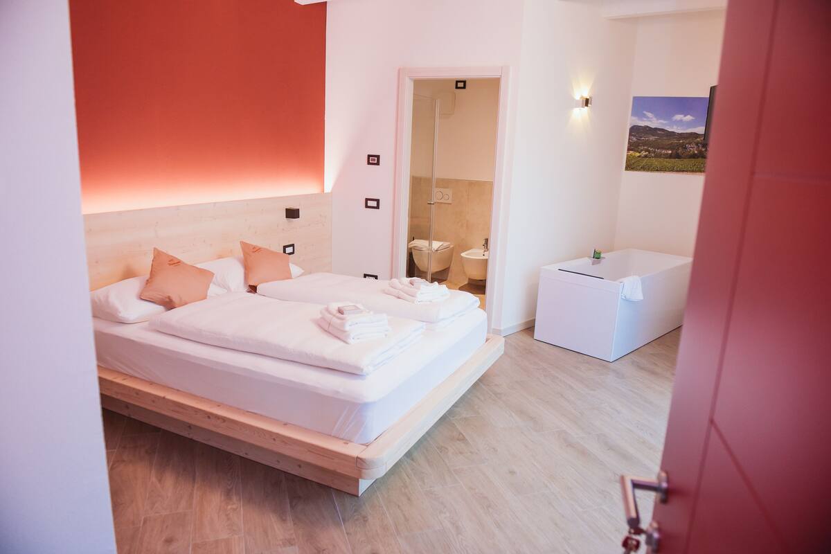 A modern bedroom with a wooden bed, a small bedside table, and a bathroom visible through an open door.