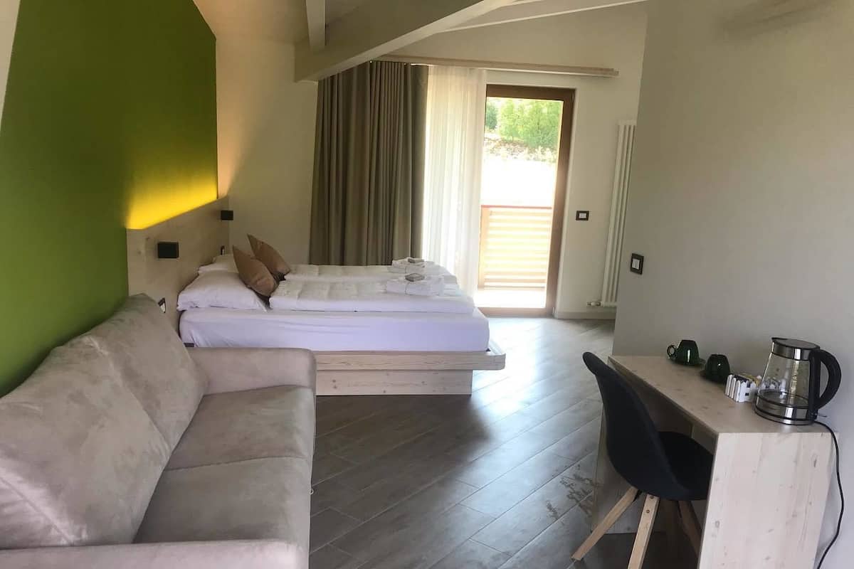 A modern room with a bed, a sofa, a desk, and a coffee maker.