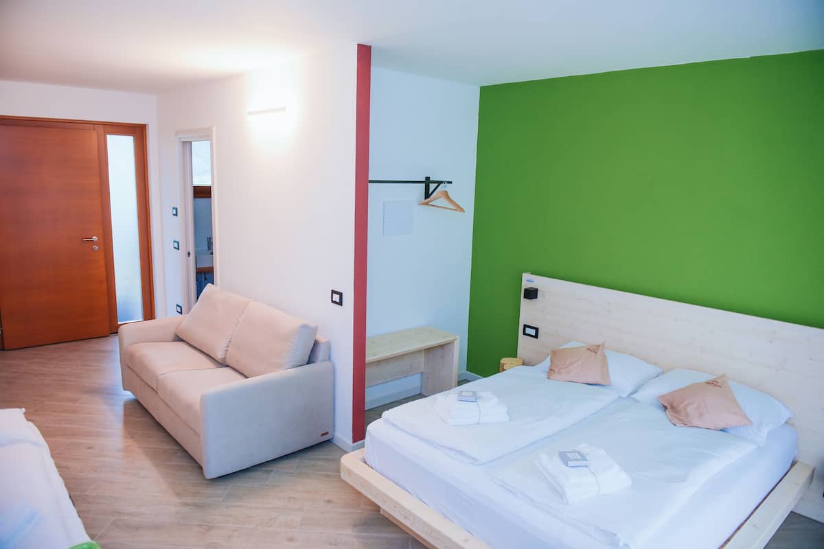 A hotel room with a bed, a sofa, a bedside table, and a green accent wall.