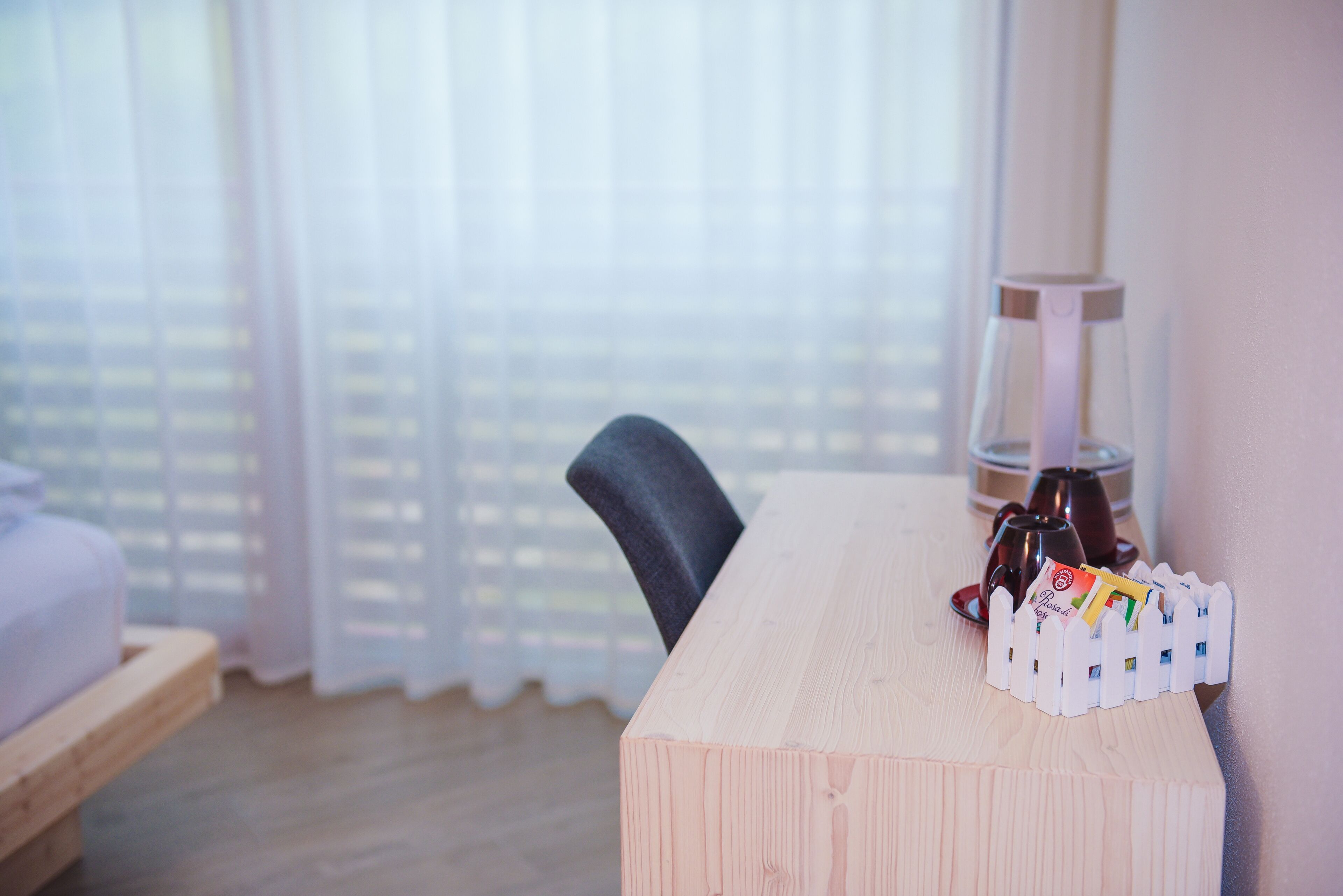 A room with a wooden desk, a chair, a lamp, and a window with curtains.