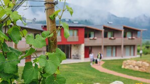 A modern building with a red facade, a stone base, and a pathway leading to a grassy area with rocks. - Agritur Verderame (Trento)