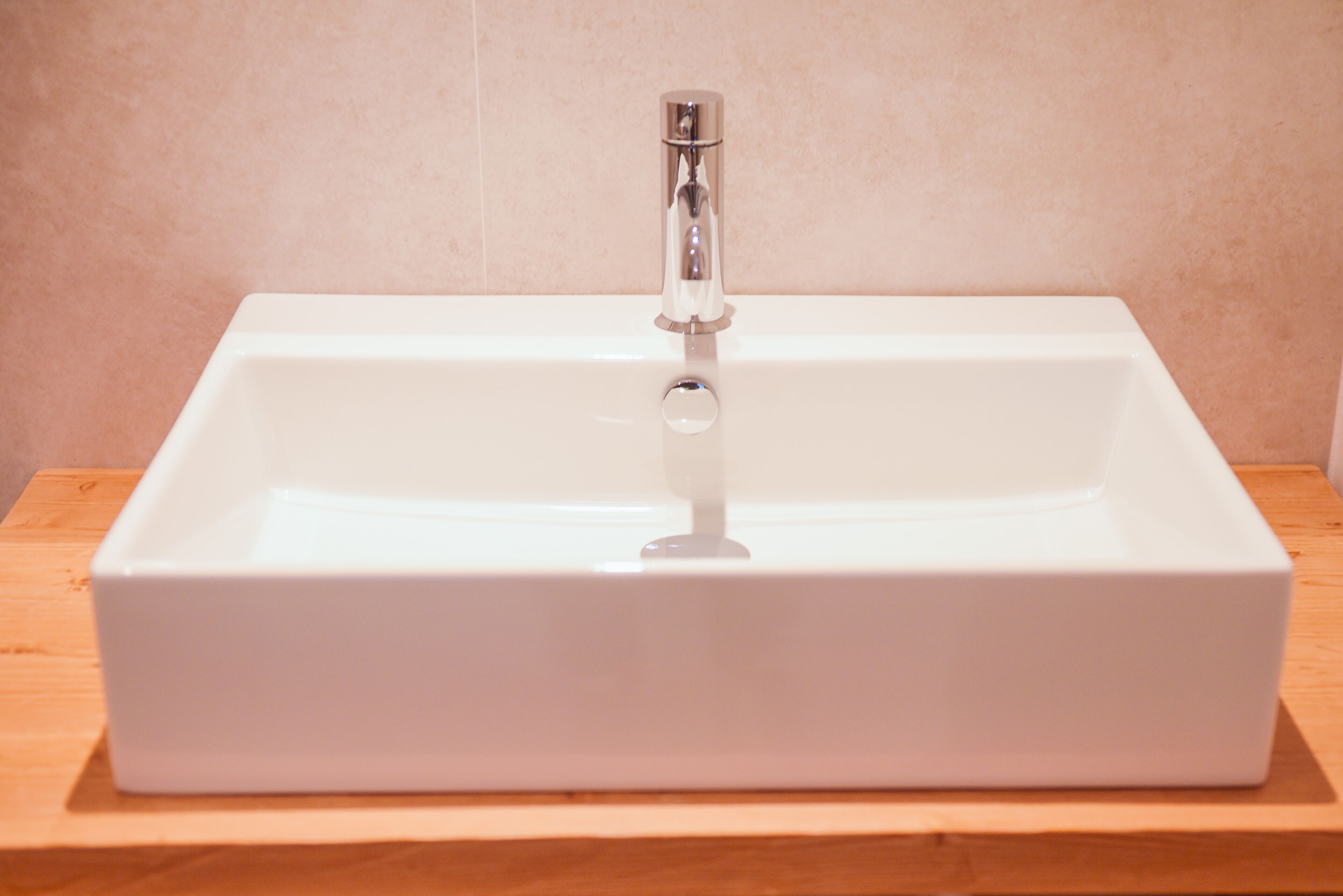 A white rectangular bathroom sink with a chrome faucet on a wooden countertop.