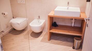Un baño moderno con un bidé, un lavamanos y un estante de madera.