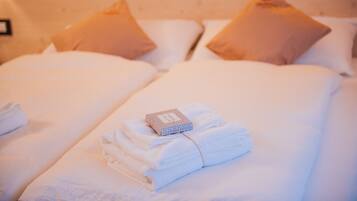 A neatly made bed with white linens and two beige pillows. A folded towel and a small box are placed on the bed.