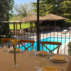 Comedor con vista a la piscina, con mobiliario de exterior y una pérgola.