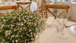 A dining area with tables set for a meal, a floral centerpiece, and a view of the outdoors through large windows.