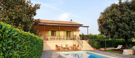 A two-story house with a swimming pool, outdoor furniture, and a well-maintained garden.