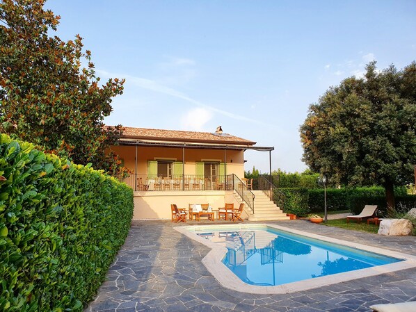Una casa de dos pisos con piscina, mobiliario exterior y un jardín bien cuidado.