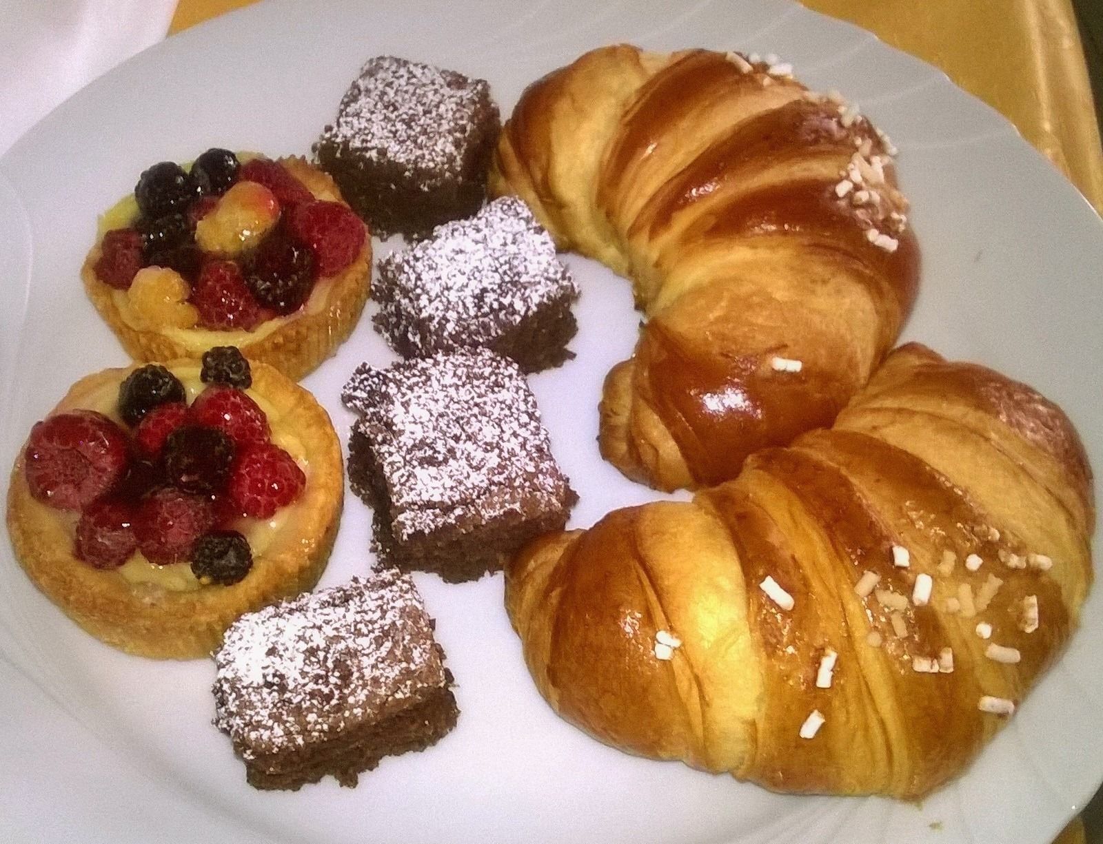 A plate with pastries including a croissant, fruit-topped pastries, and powdered sugar-dusted desserts.