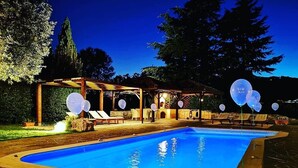 A swimming pool with lounge chairs and a pergola, surrounded by trees.