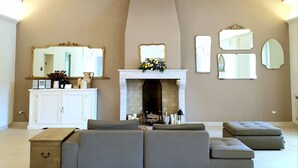 A spacious living room with a high ceiling, a fireplace, a white console table, and multiple seating options.