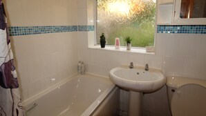 A bathroom with a bathtub, sink, and toilet. There is a window with a view of greenery outside. - Cowsley House (Derby)