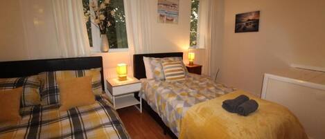 A bedroom with two beds, a nightstand, a window with curtains, and a wall-mounted picture.