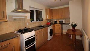 A compact kitchen with wooden cabinets, a stove, a microwave, and a washing machine. - Cowsley House (Derby)