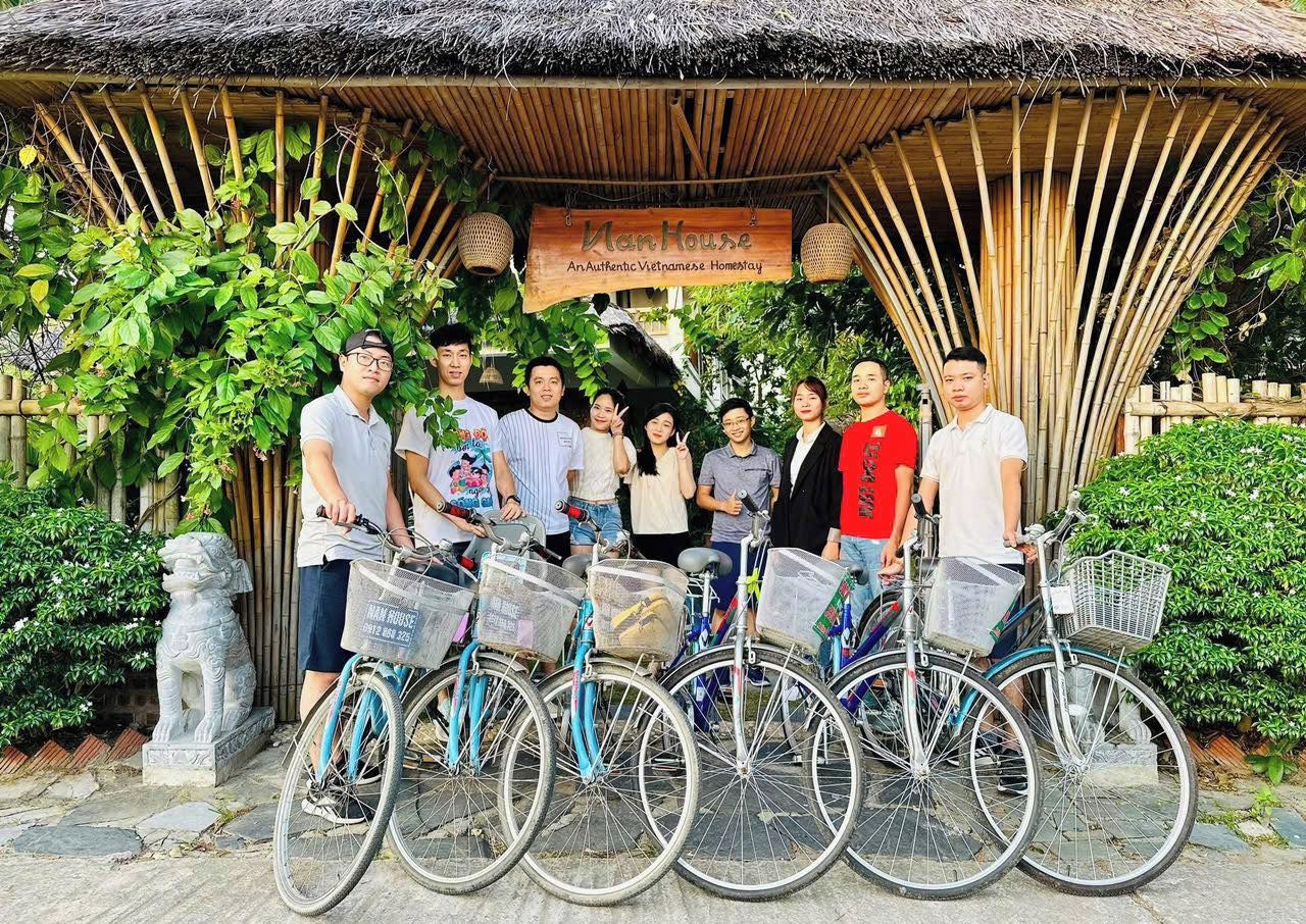 En grupp människor poserar framför en konstruktion av bambu, och en skylt bredvid lyder: ”Man House – ett autentiskt vietnamesiskt boende.”