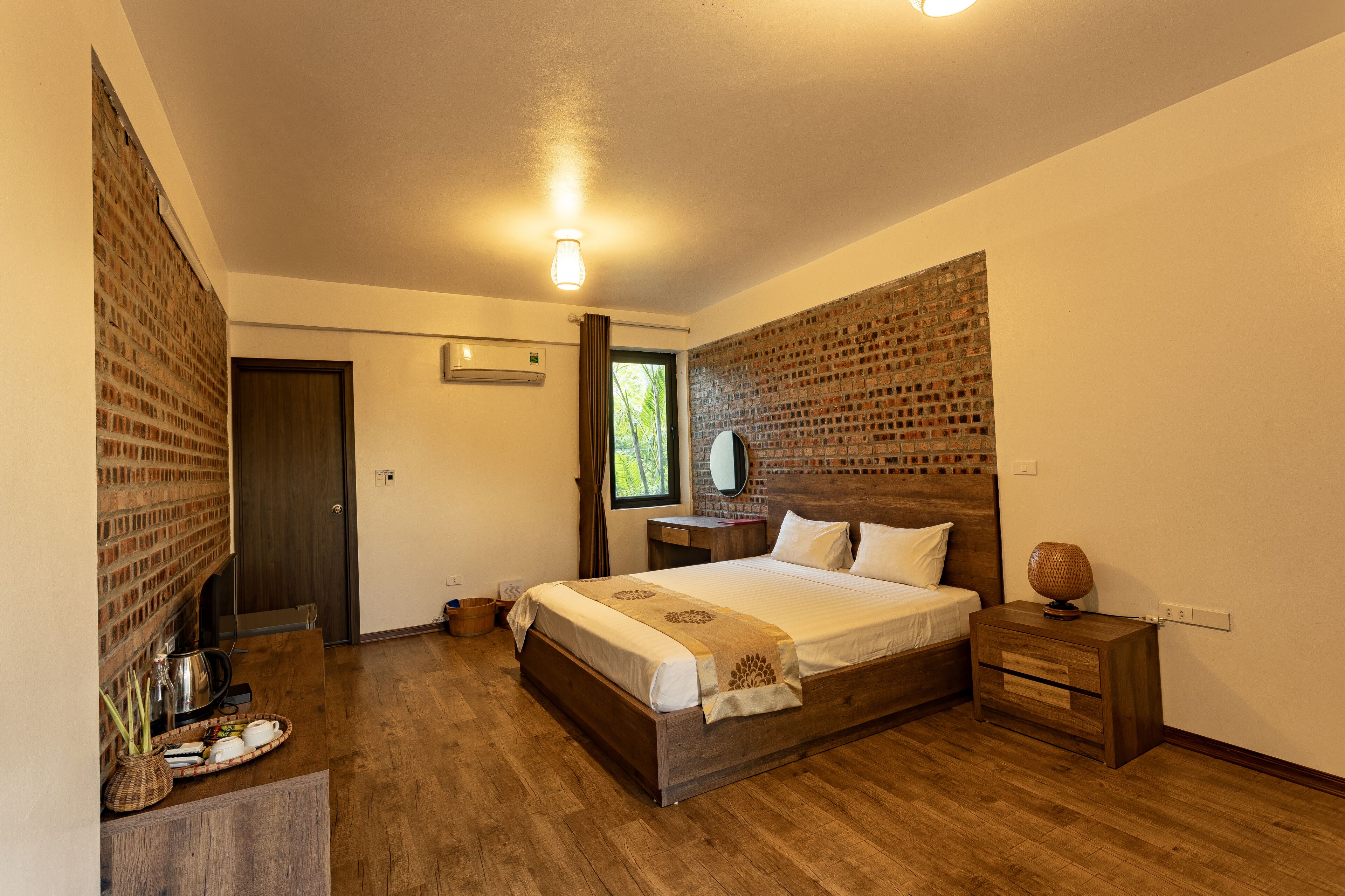 A bedroom with a wooden bed, a nightstand, a brick accent wall, and a window with curtains.