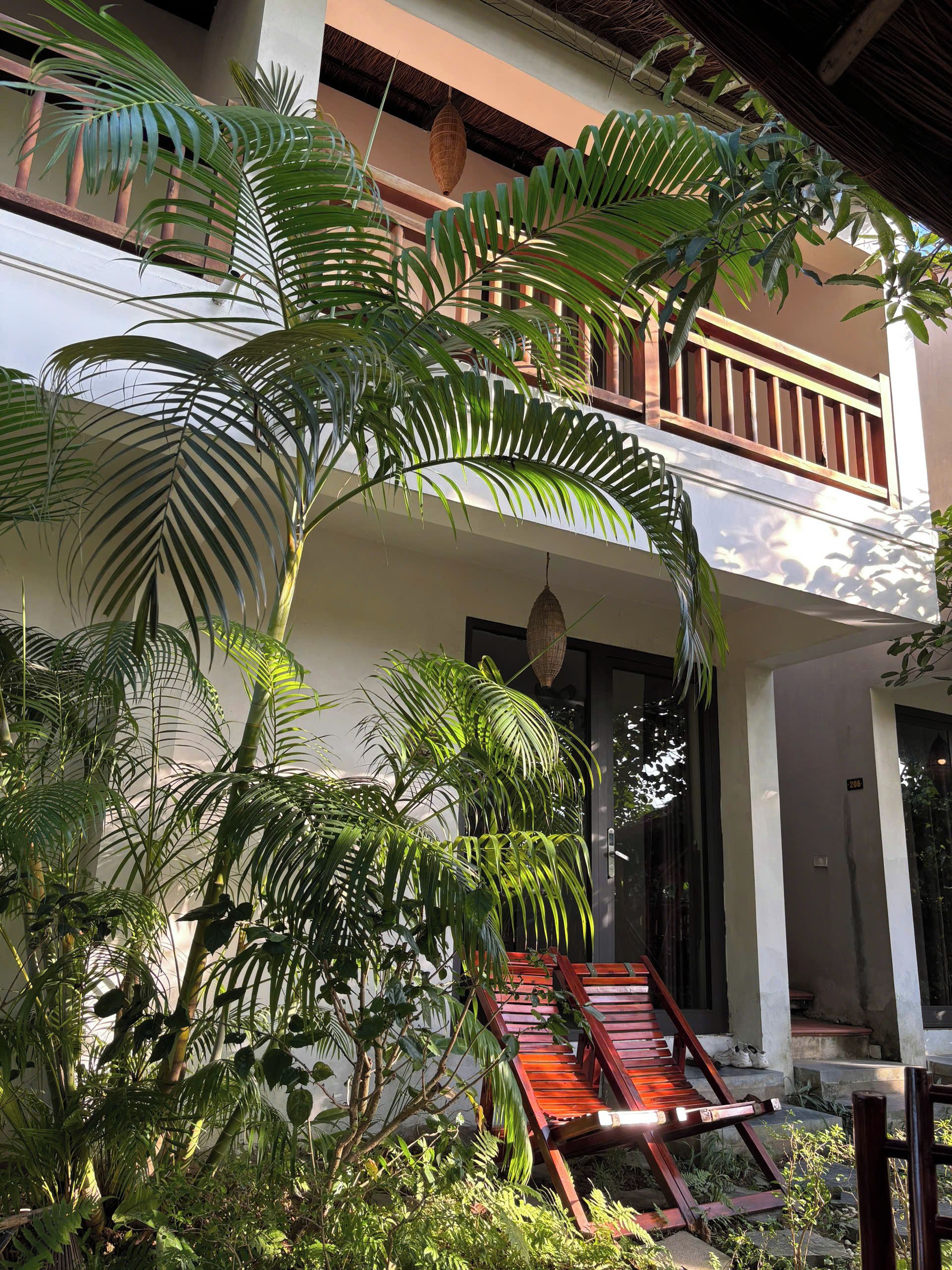 A building with a balcony, surrounded by lush greenery and a wooden deck.