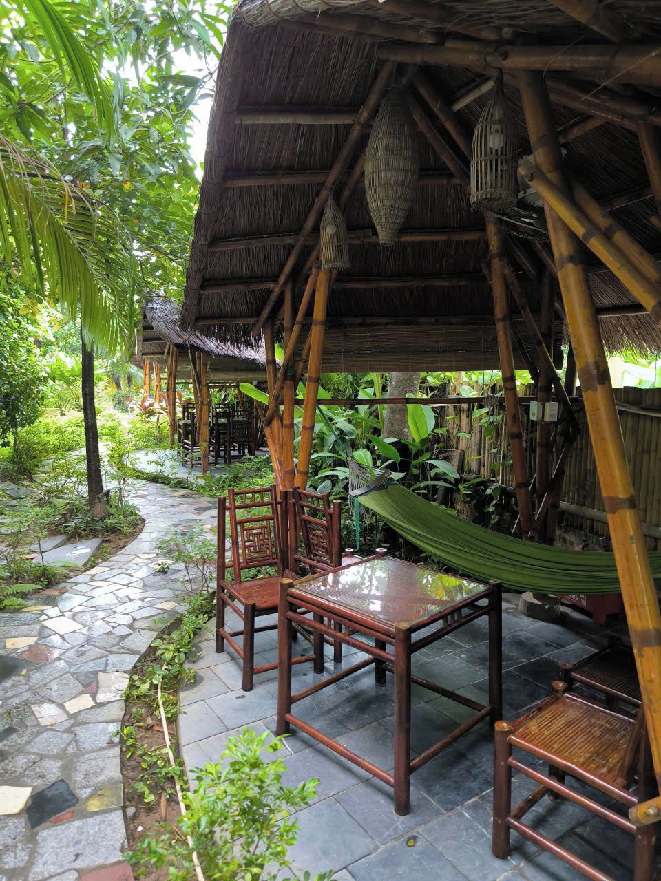 A bamboo structure with a thatched roof, a hammock, and a table with chairs.