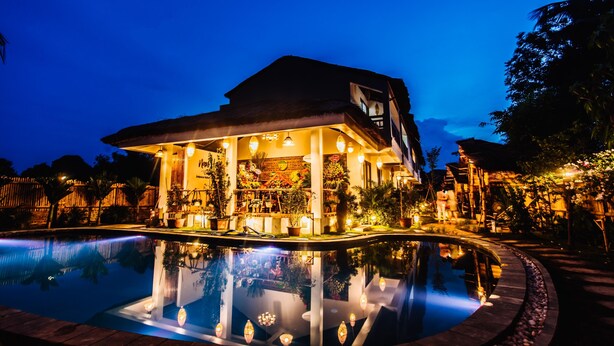 Un hotel con piscina, zona de estar al aire libre y plantas tropicales.
