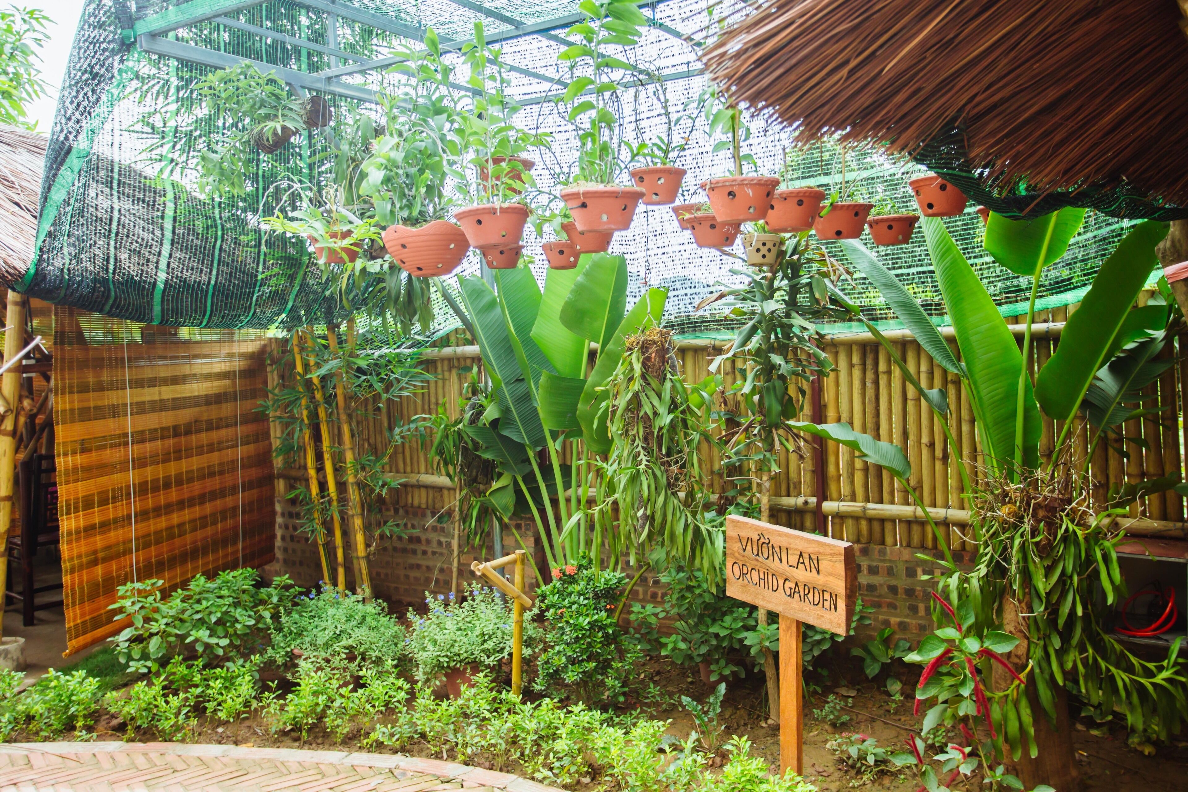 A greenhouse with hanging pots and a sign reading "Vườn Làn Orchid Garden".