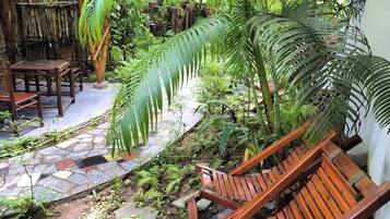 Una silla de madera para lounge en un jardín tropical con senderos de piedra y abundante vegetación.