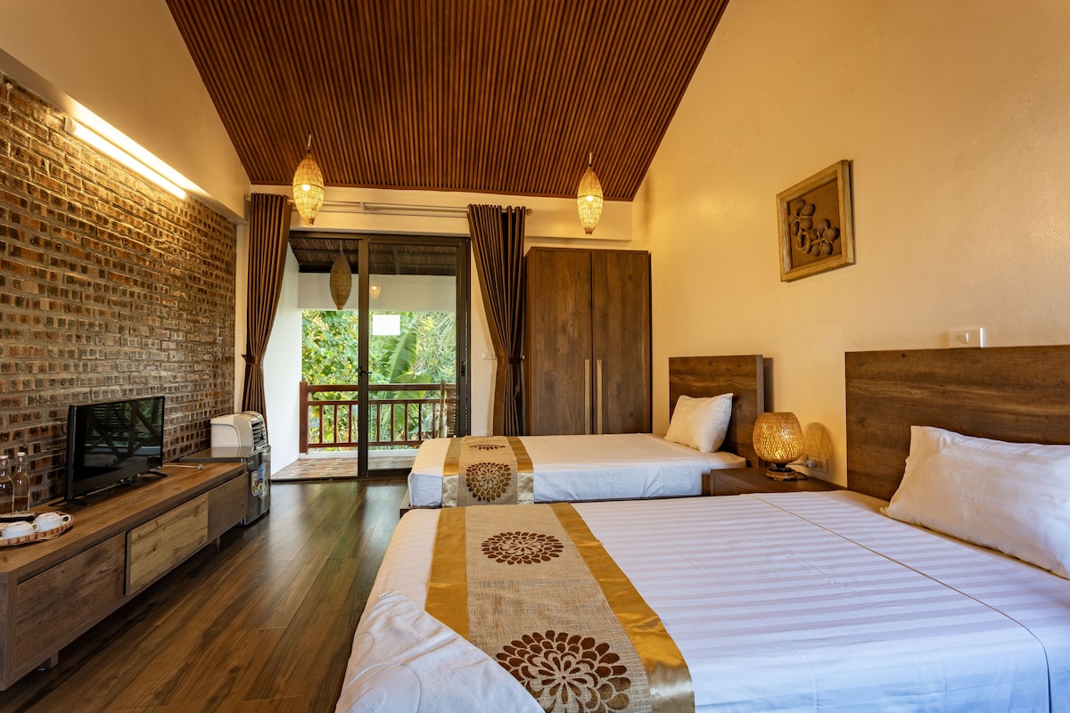 Quarto de hotel com duas camas, televisão, teto de madeira e parede de tijolos.