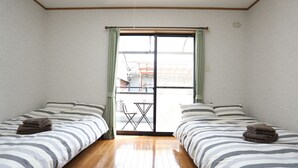 Quarto com duas camas, uma porta de correr de vidro e uma pequena mesa exterior.