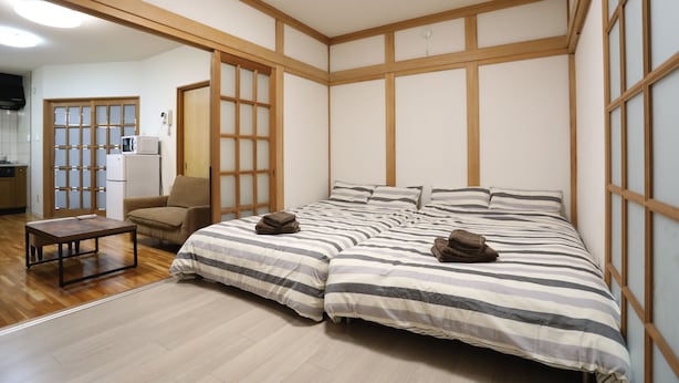 Quarto com uma cama grande, um sofá pequeno, piso de madeira e uma área de cozinha equipada com geladeira e micro-ondas.
