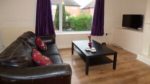 A living room with a leather sofa, a coffee table, a TV, and a window with purple curtains. - Beckley House (Nottingham)