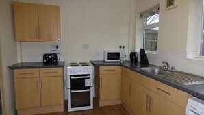 A compact kitchen with wooden cabinets, a stove, a microwave, and a sink. - Beckley House (Nottingham)