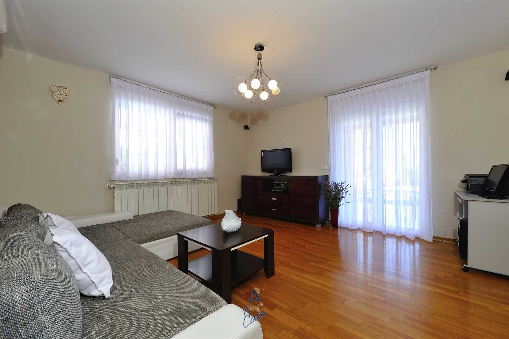 A living room with a sofa, a coffee table, a TV on a stand, and a radiator.