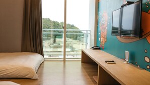 A hotel room with a bed, a desk, a TV, and a view of a cityscape through a large window.