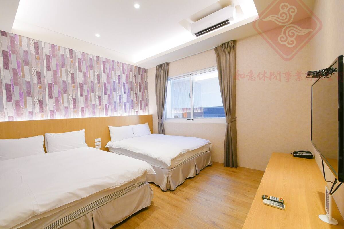A hotel room with two beds, a wooden desk, a TV, and a window with curtains.