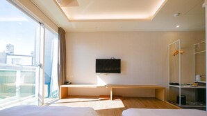 A hotel room with two beds, a TV mounted on the wall, a desk, and a large window offering a view of the city.
