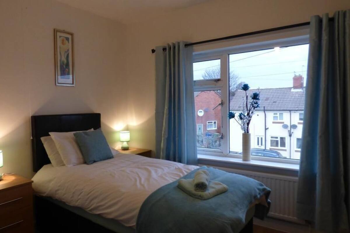 A bedroom with a bed, bedside lamps, a window with curtains, and a view of buildings outside.