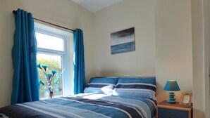 Een slaapkamer met een bed, een nachtkastje, een lamp en een schilderij aan de muur.
