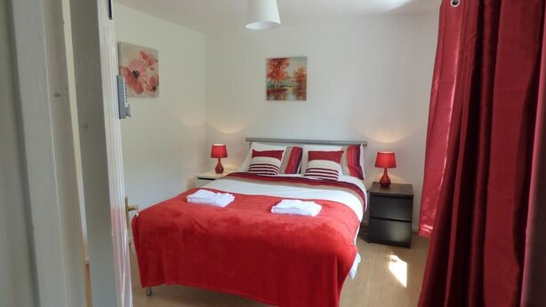 A bedroom with a bed, two bedside tables, and red curtains.