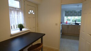 A hallway leading to a kitchen with a window, a table, and a basket.