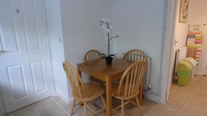 A dining area with a wooden table and four chairs, a potted orchid, and a white door.
