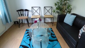 A living room with a glass coffee table, two chairs, a black sofa, and a potted plant.