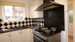 A kitchen with white cabinets, a black stove, and a window with a view of buildings outside. - Boythorpe House (Chesterfield)