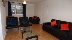 A living room with two black leather sofas, one with red and one with blue cushions, a glass coffee table, and a window with curtains. - Boythorpe House (Chesterfield)