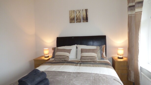 A neatly made bed with striped bedding, two bedside lamps, and a headboard. - Boythorpe House (Chesterfield)