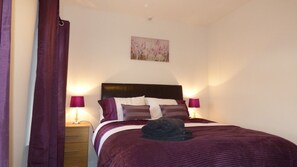 A neatly made bed with a dark headboard, two bedside lamps, and a single artwork above the bed. - Boythorpe House (Chesterfield)