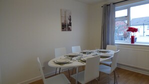 A dining area with a table set for four, white chairs, and a window with a view of buildings. - Boythorpe House (Chesterfield)