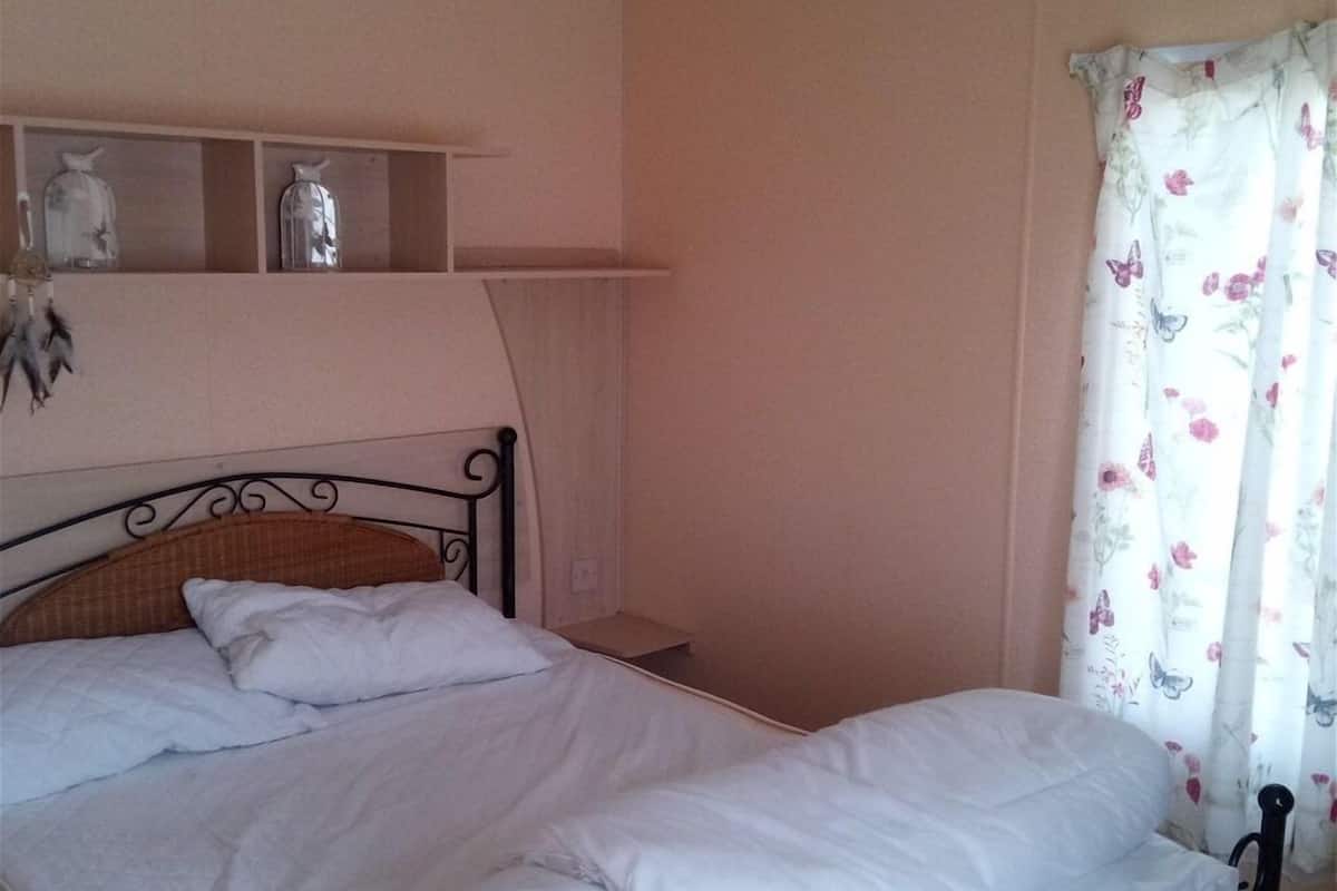 Ein Schlafzimmer mit einem Einzelbett, einem Nachttisch, einer Ablage mit Dekoration und einem Fenster mit blumigen Vorhängen.
