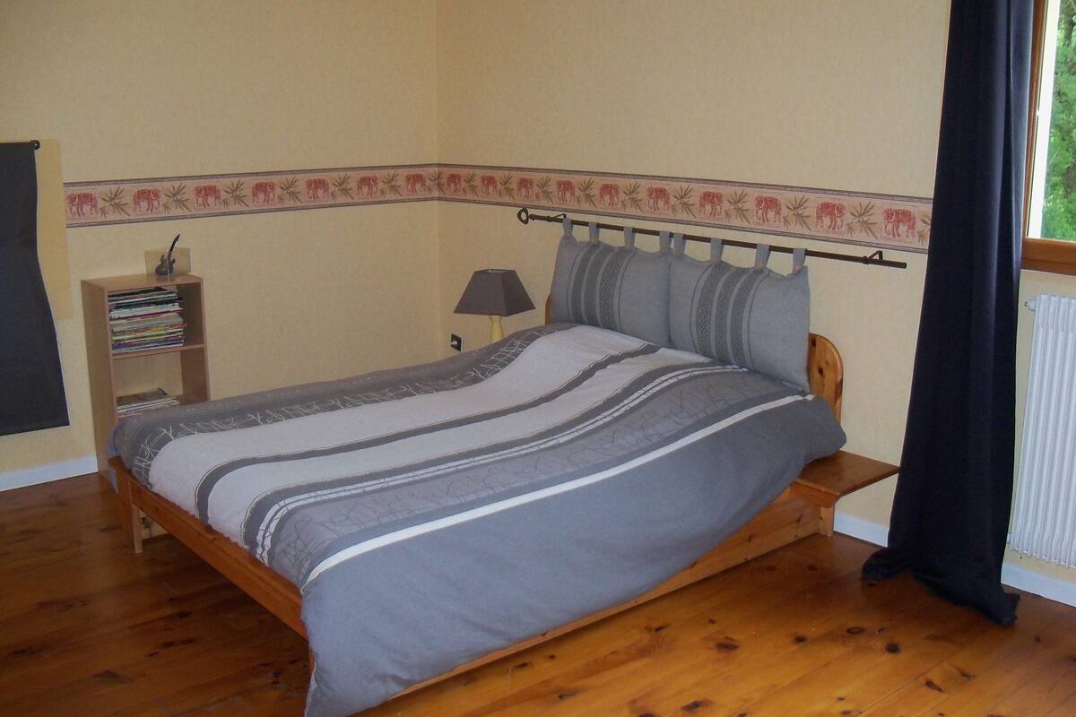 A bedroom with a wooden bed, a nightstand with a lamp, a bookshelf, and a window with curtains.