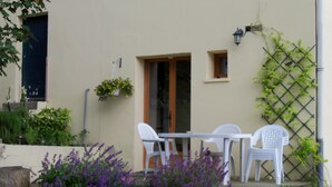 A patio with white plastic chairs and a table, surrounded by purple flowers and greenery. - Chambre D'hote et Gite Le Parc (Revel)