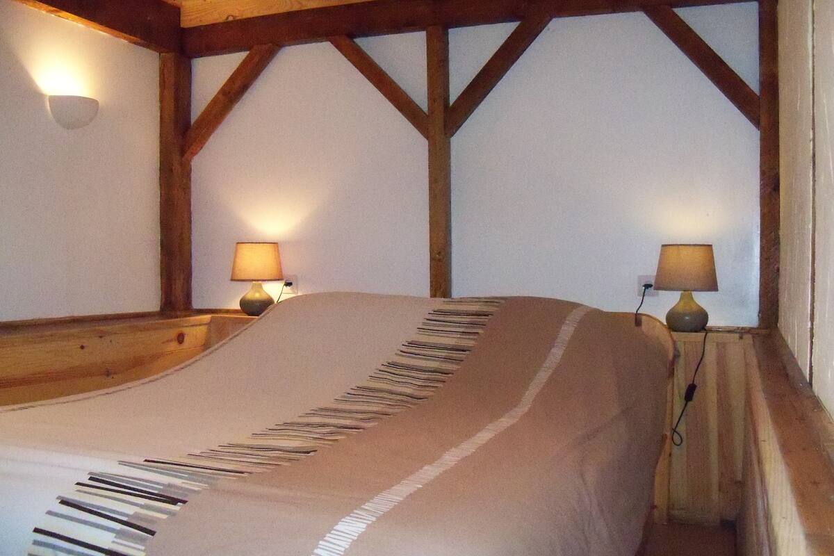 A room with a bed, wooden beams, two wall-mounted lamps, and a white wall.