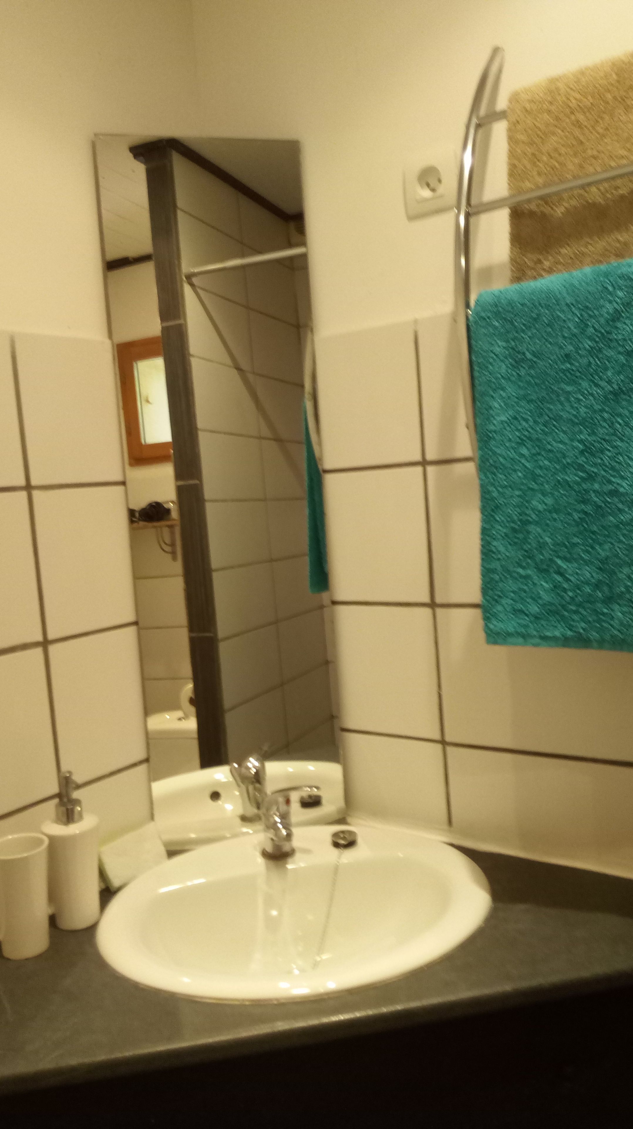 A bathroom with a white sink, a mirror, a towel rack with a blue towel, and a shower visible in the background.